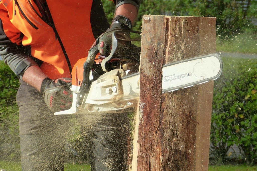 Ein Holzfäller schneidet im Freien mit einer Kettensäge einen Baumstamm und präsentiert dabei professionelle Ausrüstung sowie Schutzkleidung.