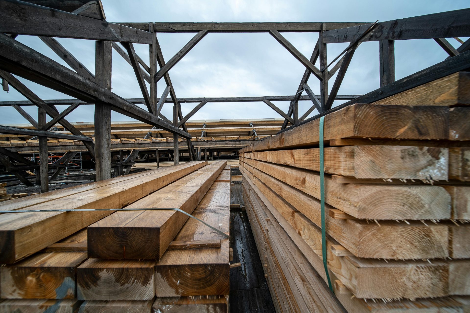 Gestapelte Holzbohlen auf einem industriellen Außenlagerplatz unter einem bewölkten Himmel.